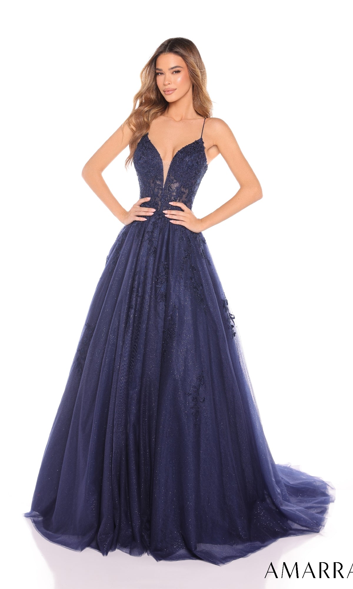 A woman wearing the Amarra 88410 prom ball gown?a deep navy blue, floor-length designer dress with a corset bodice, thin straps, and plunging neckline?stands against a white background.